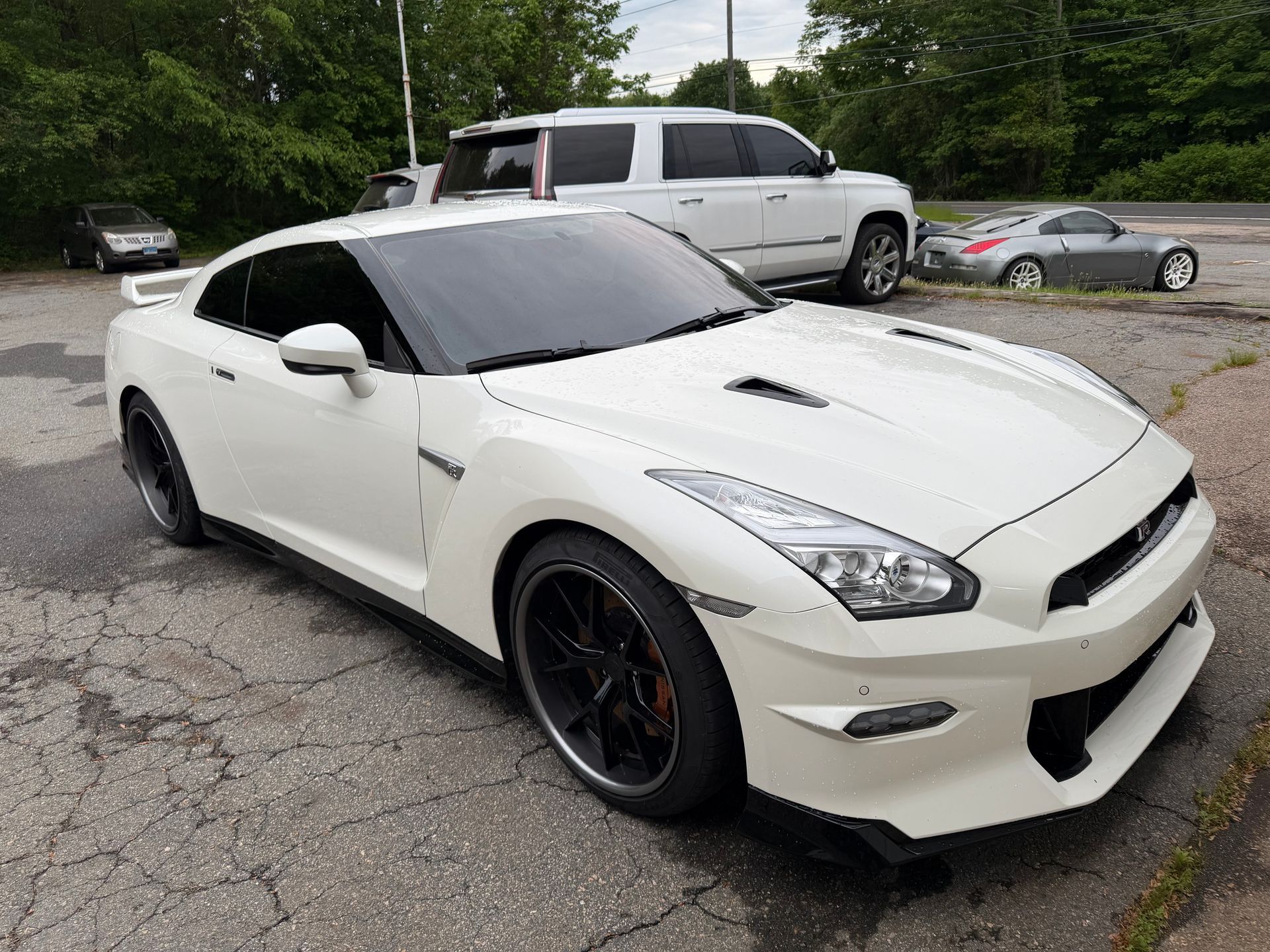White sports coupe parked on a cracked driveway beside a white pickup truck and gray sedan
