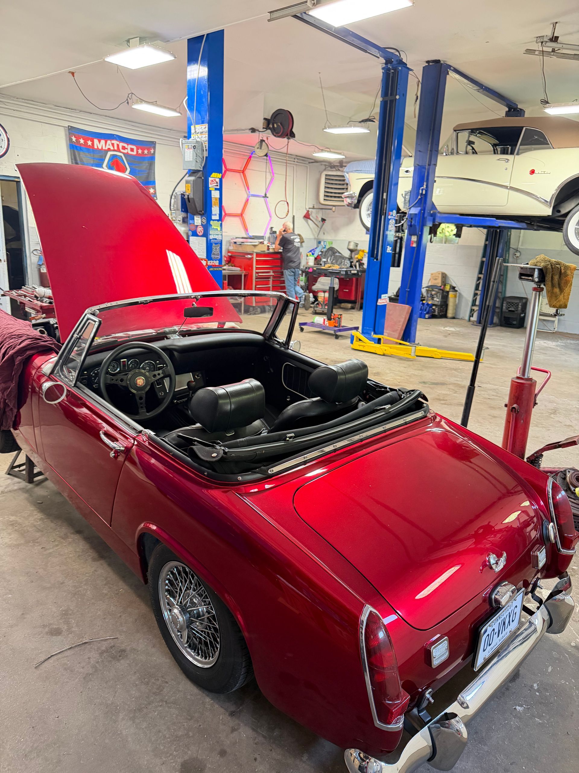 Red classic convertible with top down and hood open in an auto repair garage