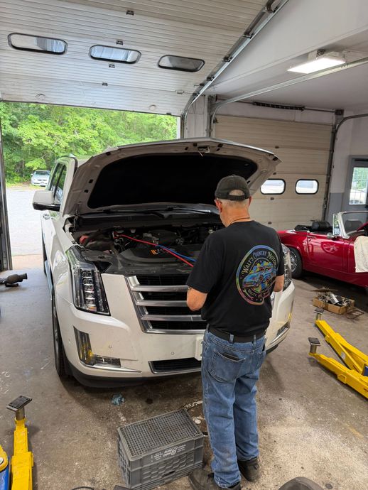 Person inspecting a white SUV with open hood inside an auto repair shop, yellow lift nearby