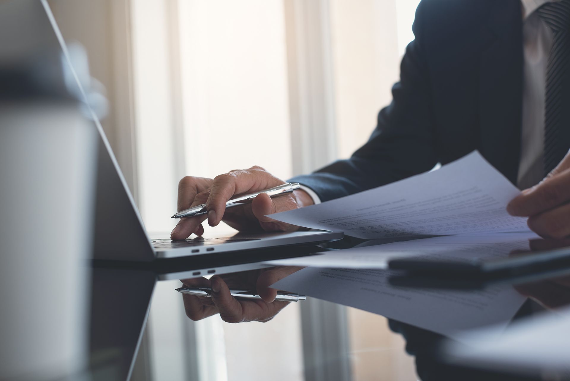 A man is sitting at a desk using a laptop computer and a pen.