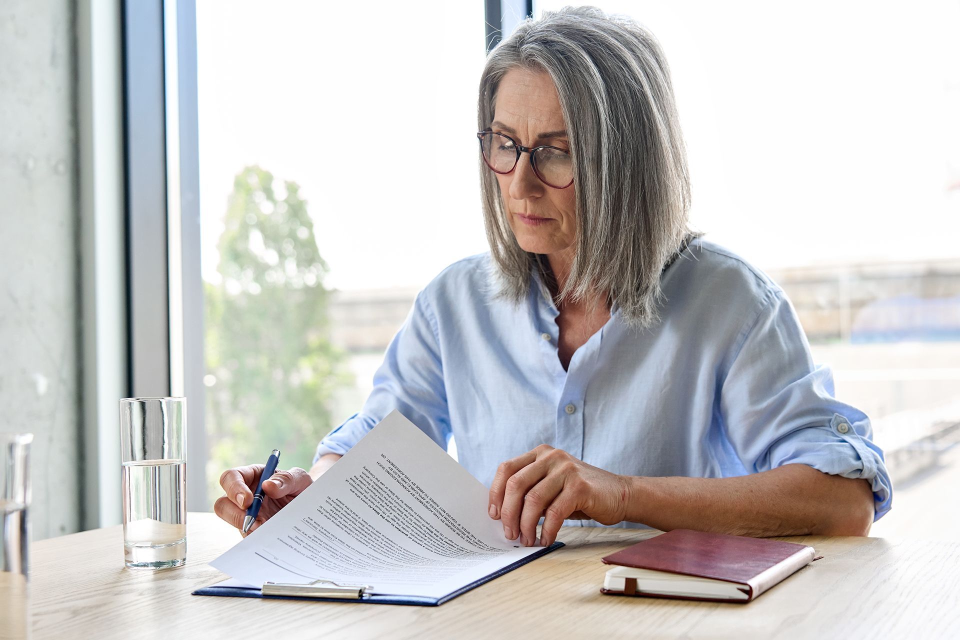 An older woman is sitting at a table looking at a piece of paper.