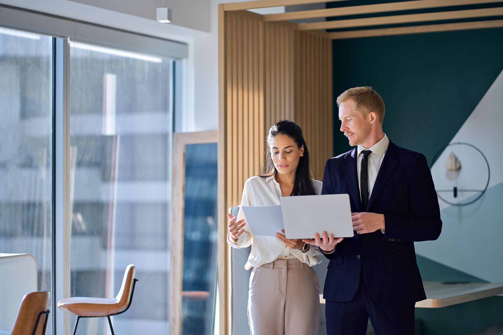 A man and a woman are looking at a piece of paper in an office.