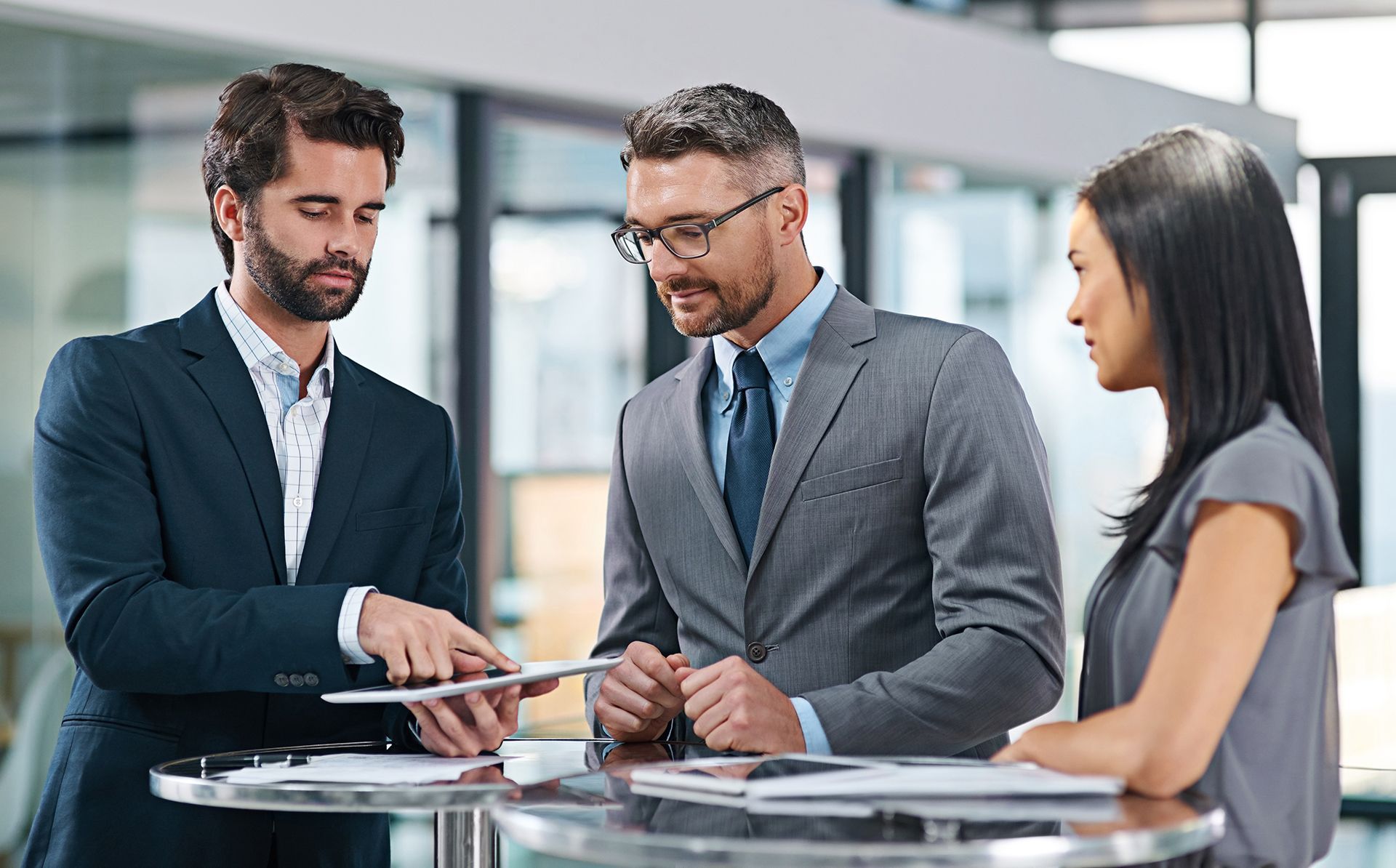 A group of business people are standing around a table looking at a tablet.