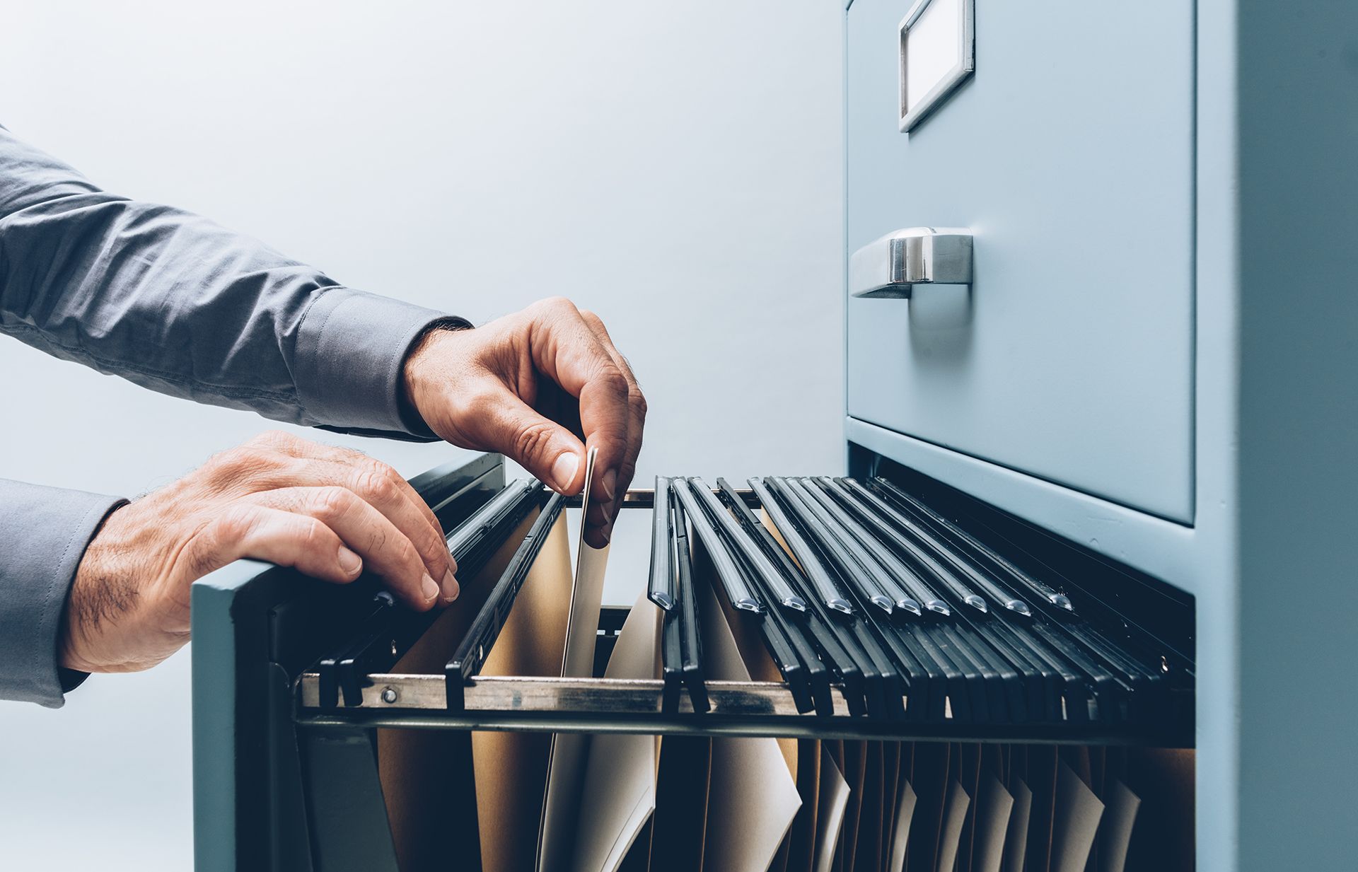 A man is taking a file out of a filing cabinet.