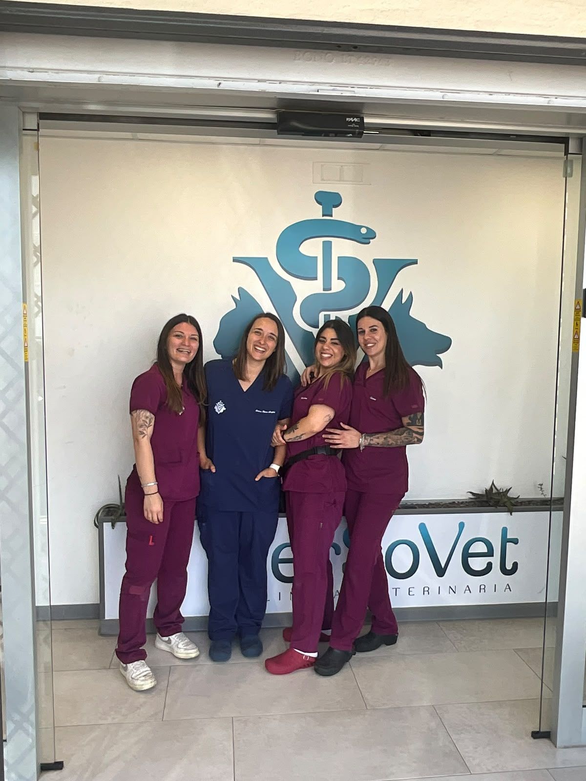 Quattro veterinari in camice chirurgico in piedi insieme davanti all’insegna di una clinica veterinaria.
