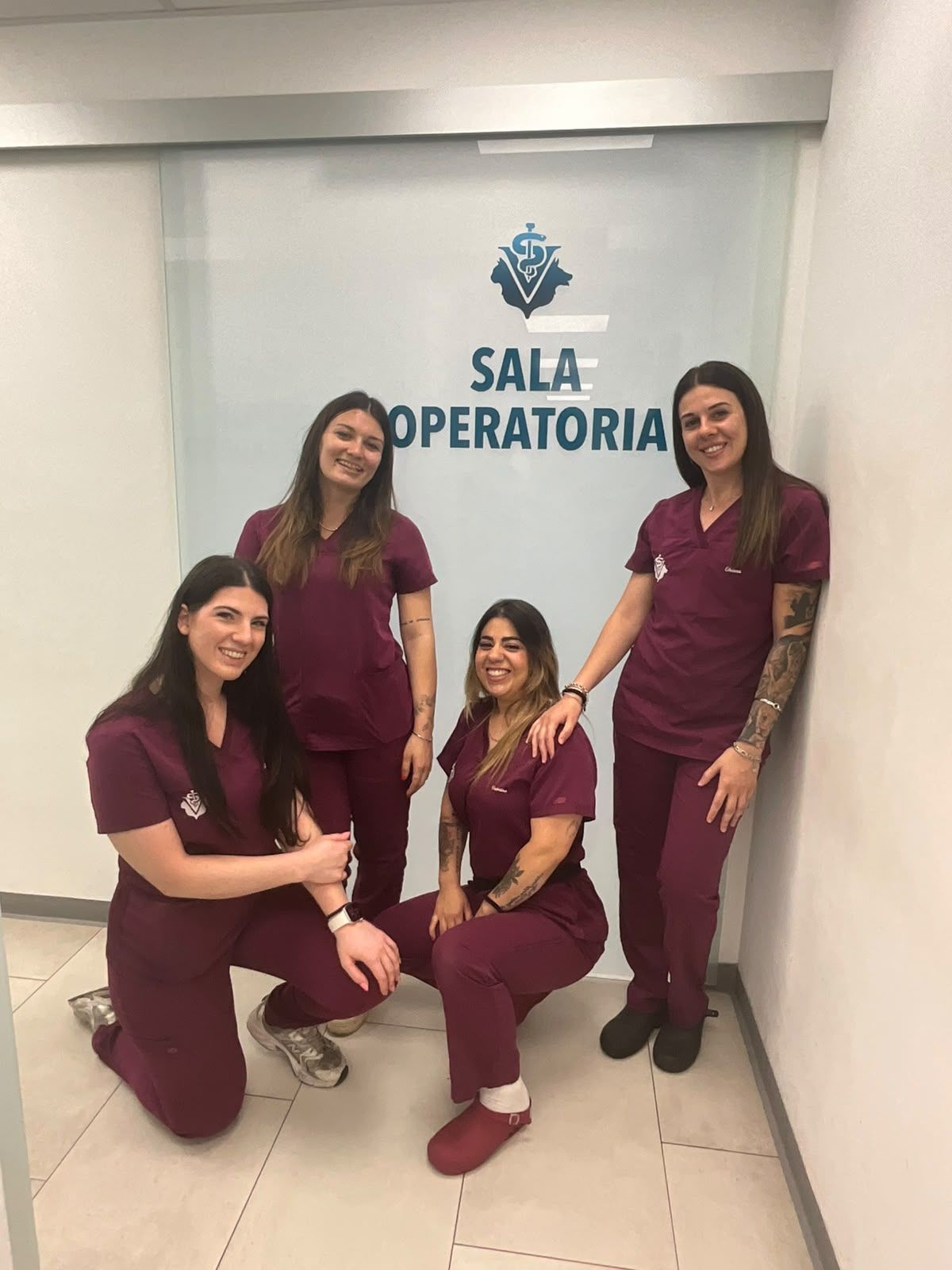 Quattro persone in divisa chirurgica bordeaux posano davanti a un cartello con la scritta “Sala Operatória”
