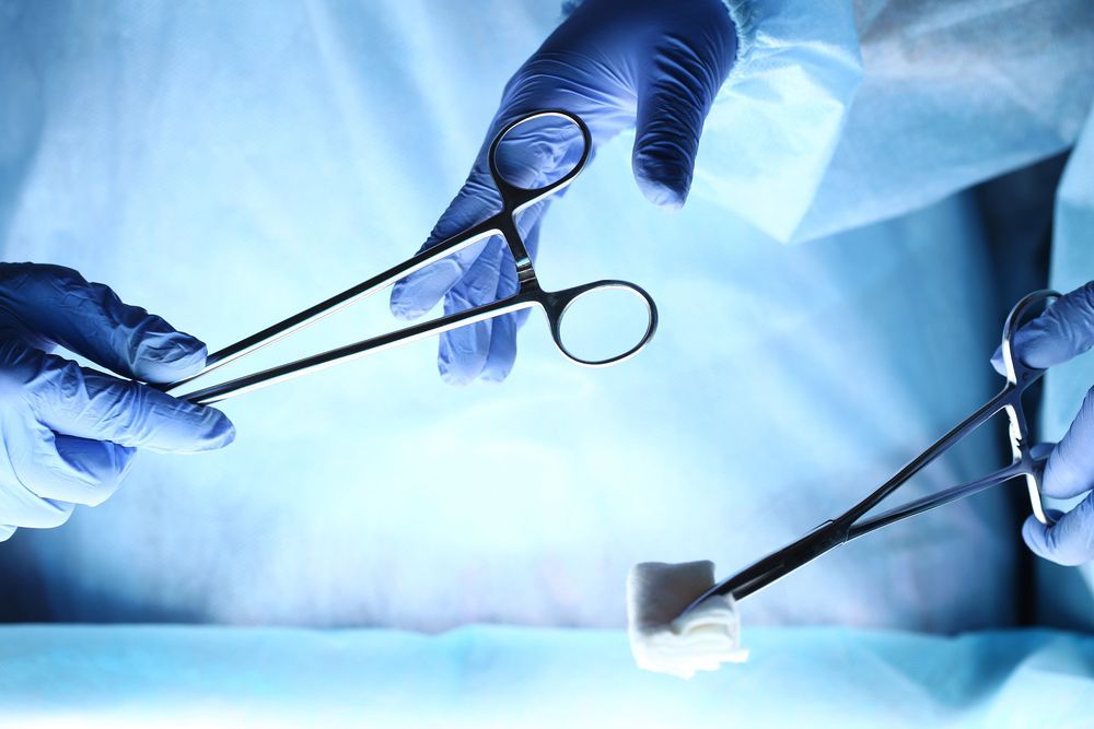 Chirurghi con i guanti che utilizzano strumenti durante un intervento chirurgico illuminato da una luce blu intensa in una sala operatoria.
