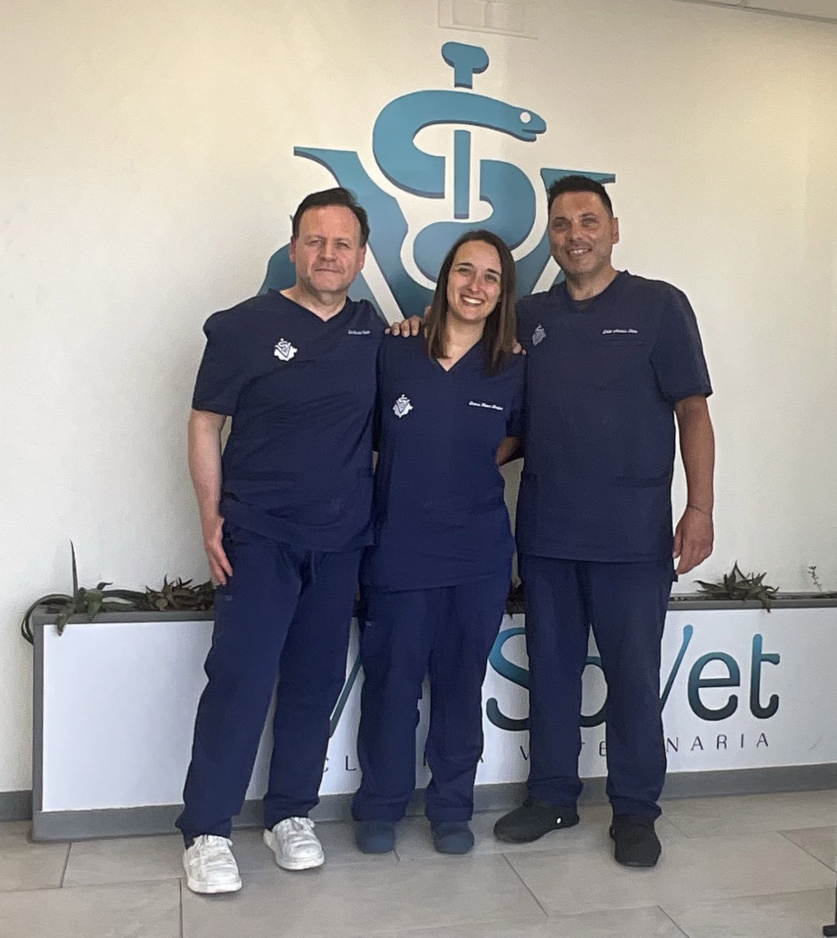 Tre membri dello staff vestiti di blu navy sorridono davanti all’insegna di una clinica.