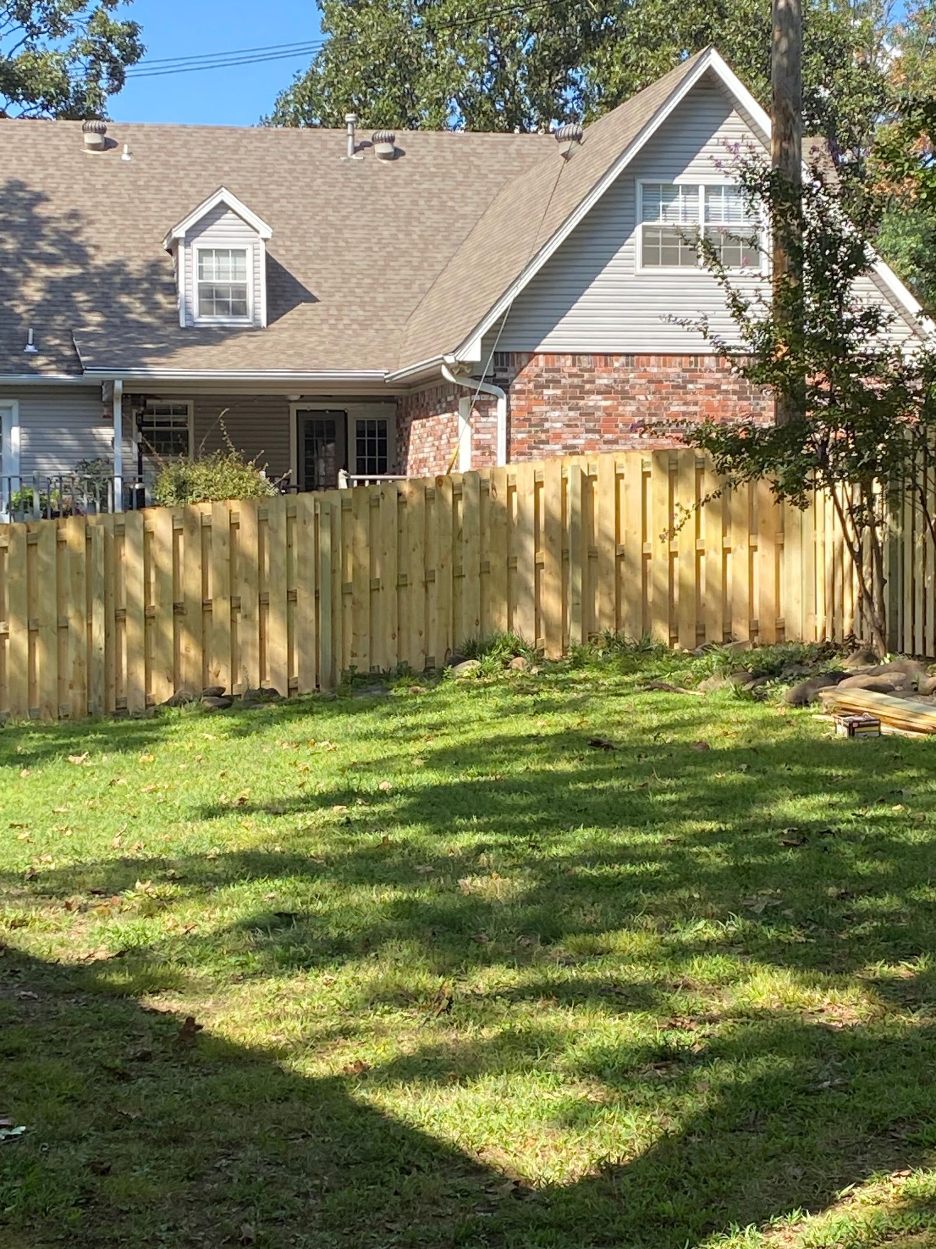 Wooden fence bordering a grassy backyard; a house with a brick facade is visible behind it.