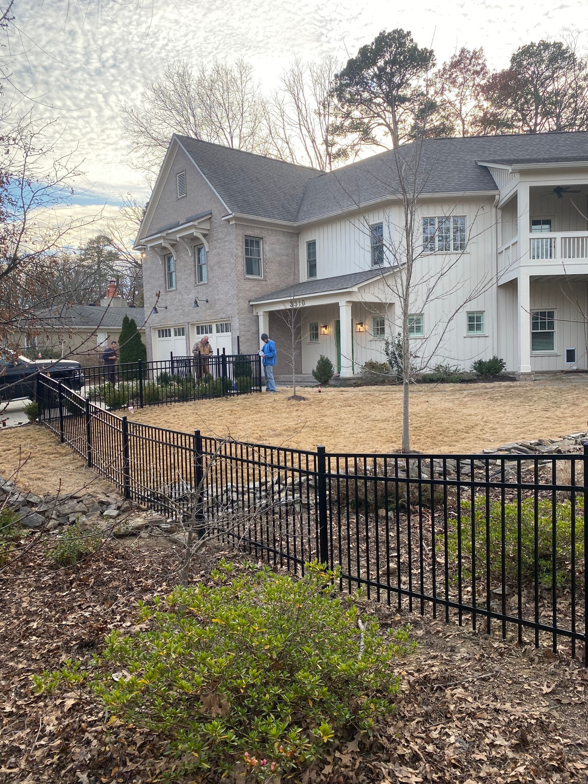 Two-story house with light brick and white siding, black fence, and bare yard.