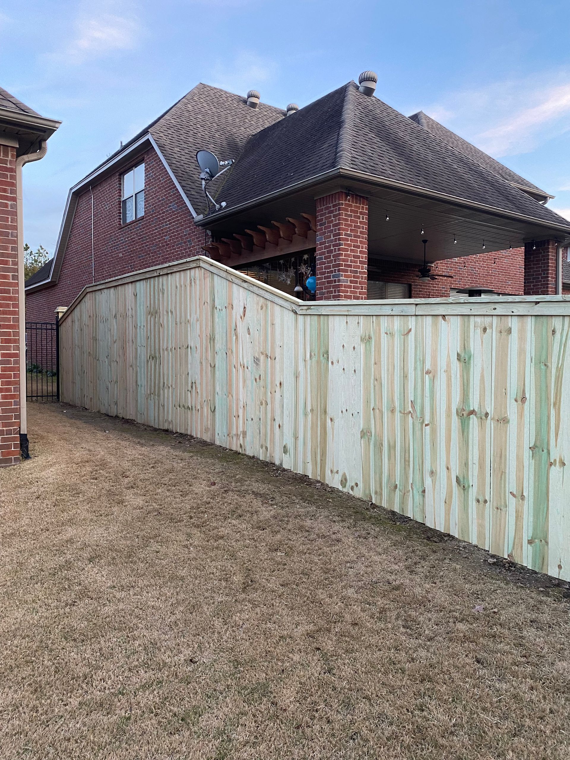 A new wooden fence surrounds a brick house with a covered patio.