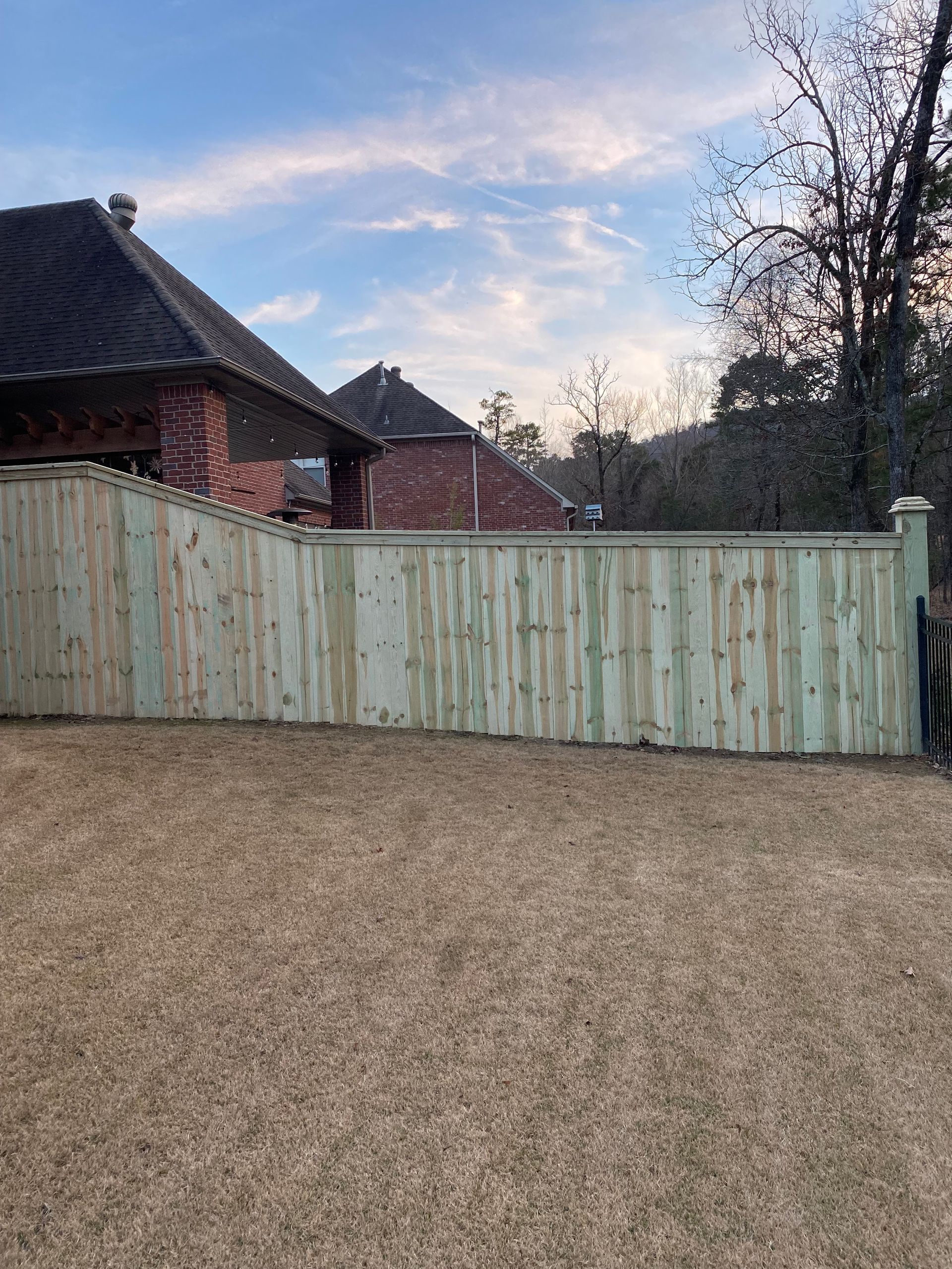 Wooden fence around a grassy yard, partially in front of a brick house under a blue sky.
