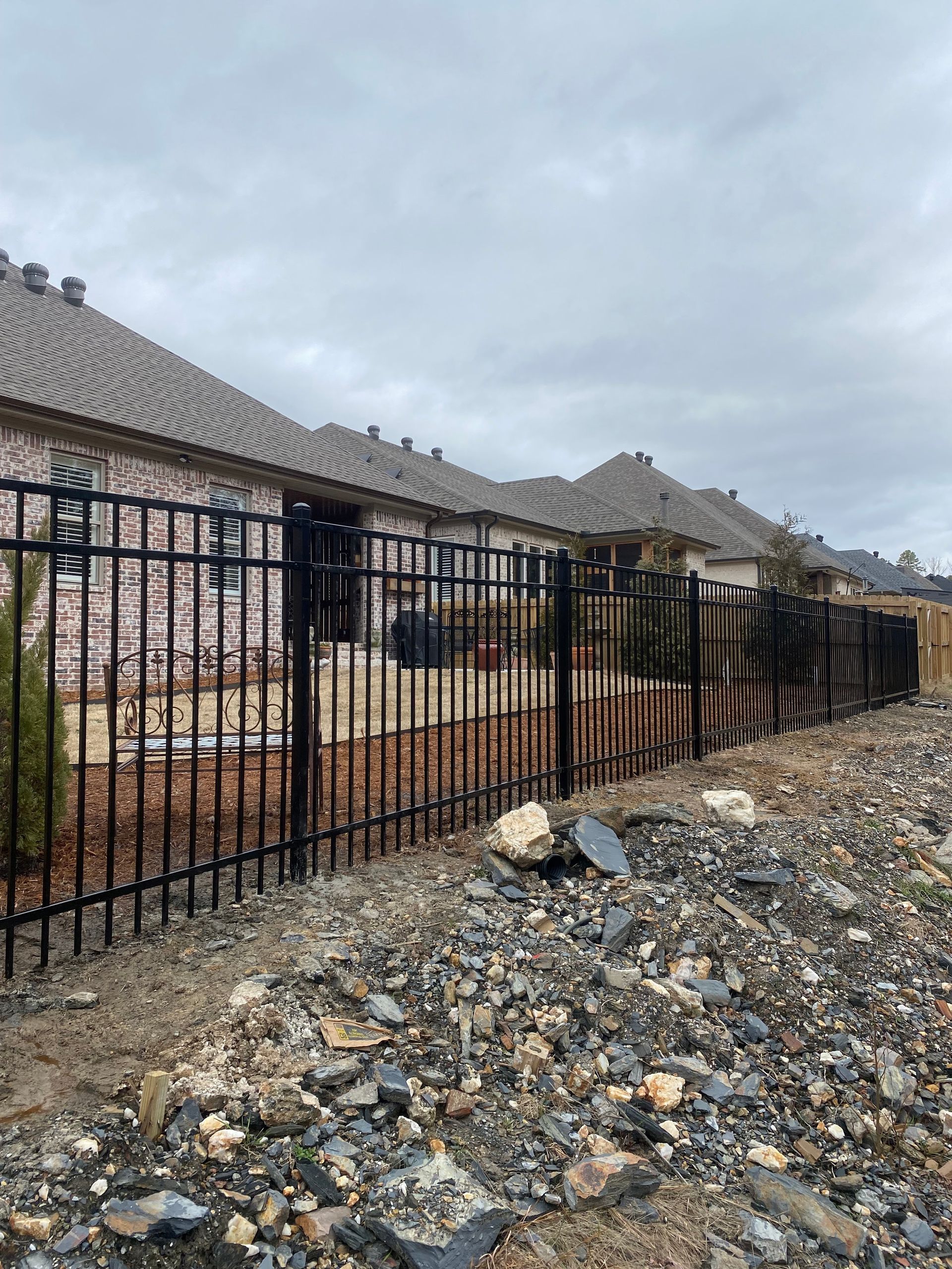 Black metal fence in front of brick buildings on an overcast day, with debris in the foreground.