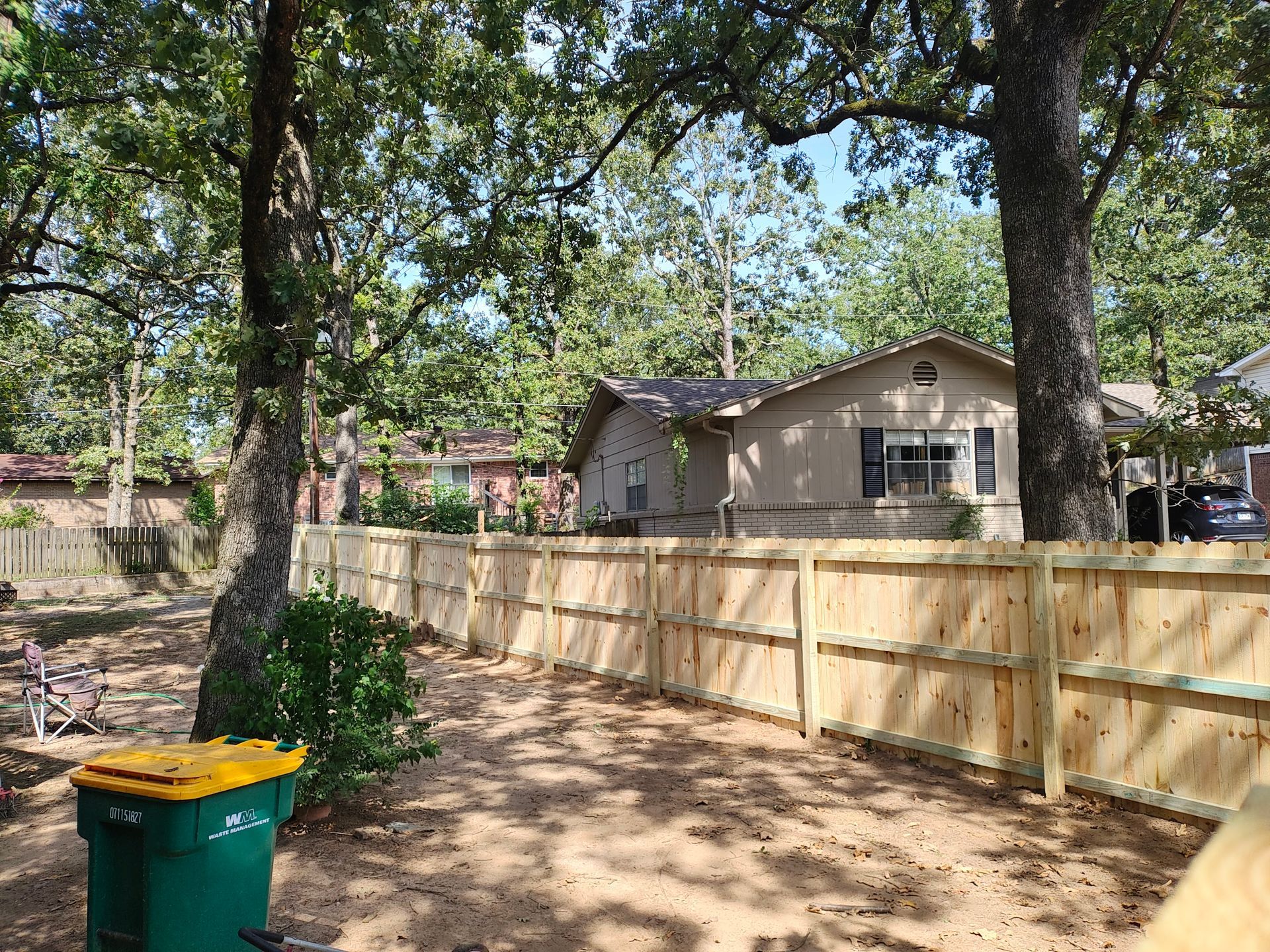 Wooden fence enclosing a yard with trees, a house, and a trash can.