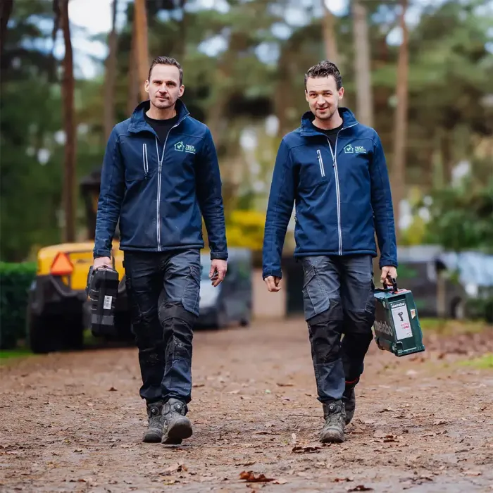 Twee mannen van Tech Green in blauwe jassen lopen over een onverharde weg.