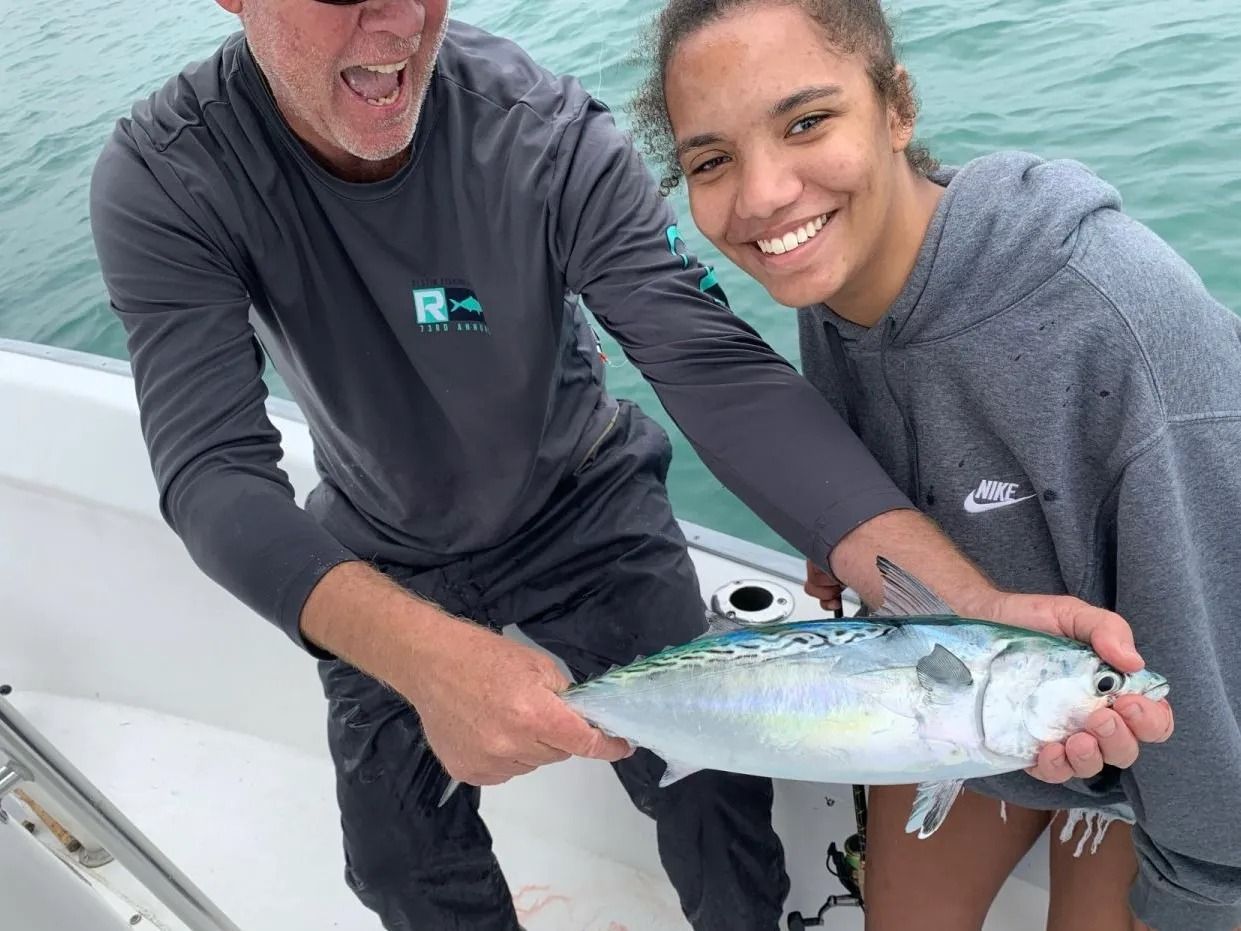 Two people smile while holding a freshly caught fish on a boat on the water.
