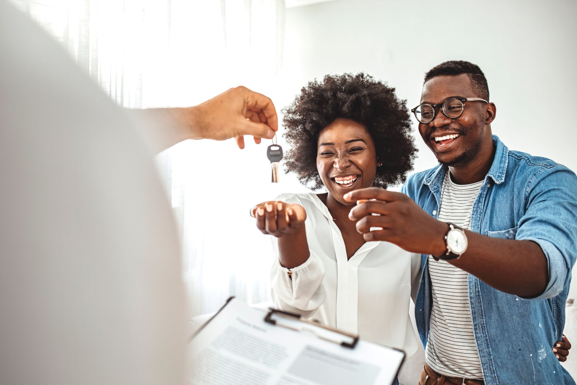 A person hands a set of keys to a smiling couple in a bright room, representing a successful real estate transaction.