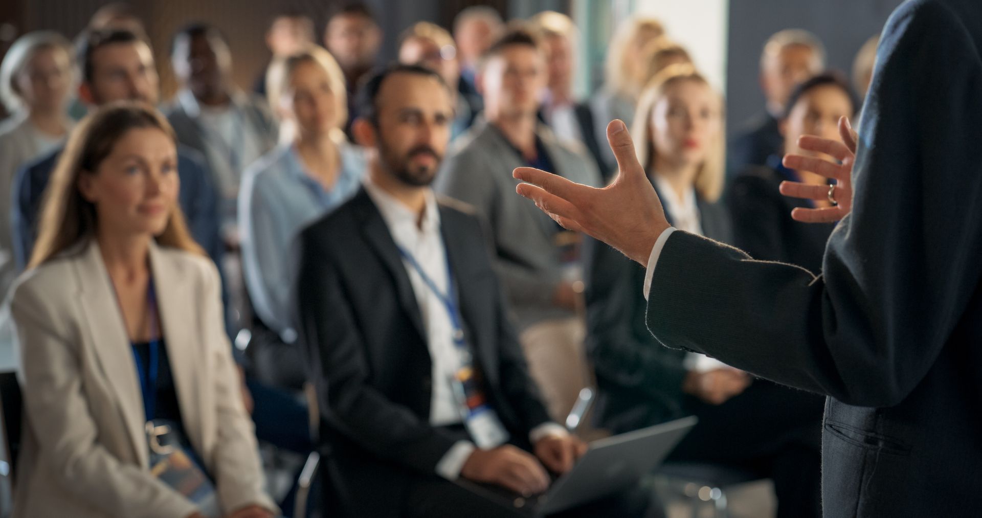 A speaker gesturing to an engaged audience in a professional conference room setting.