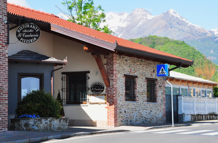Edificio in pietra con tetto rosso e montagne sullo sfondo, accanto a un segnale di attraversamento pedonale tranquillo.