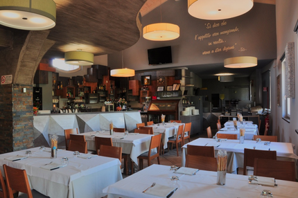 Sala da pranzo vuota di un ristorante moderno con tovaglie bianche, lampade a sospensione e un bar sullo sfondo.