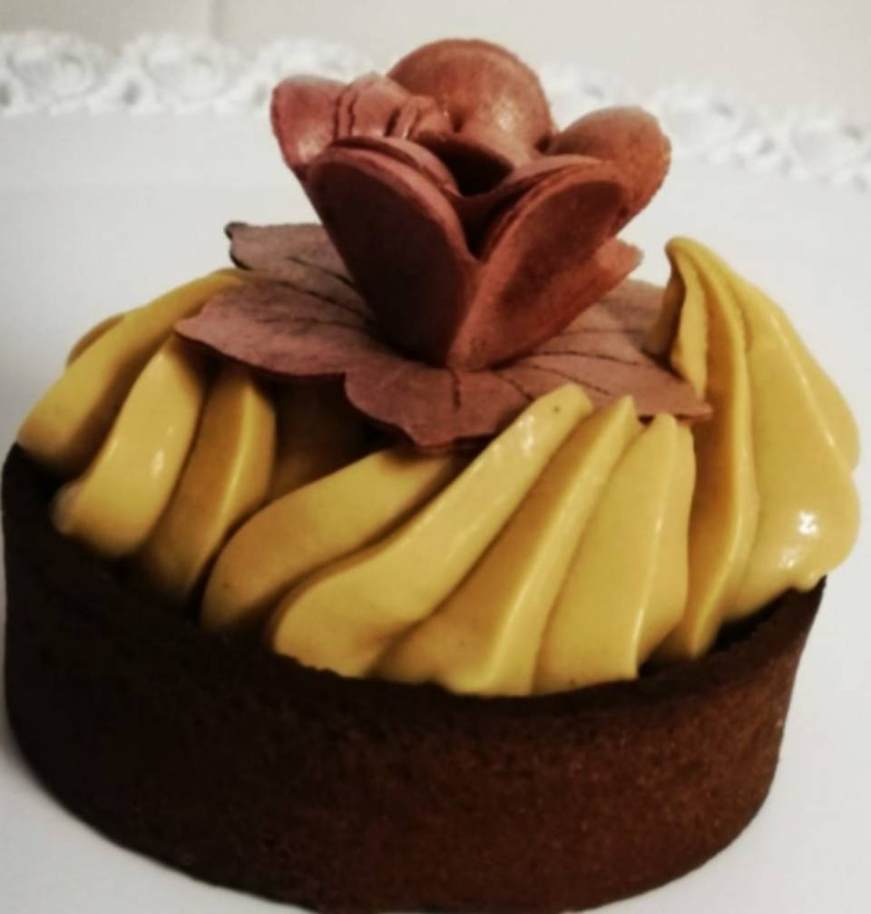 Cupcake al cioccolato con glassa gialla a spirale e decorazione floreale rosa sulla parte superiore.