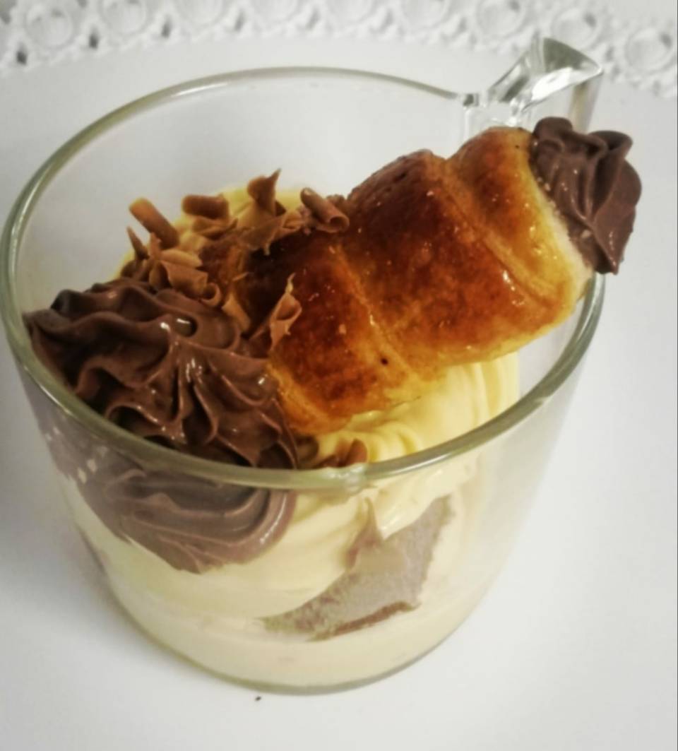 Dessert alla crema di cioccolato in una coppetta di vetro, guarnito con panna montata e una fetta di torta al caramello.