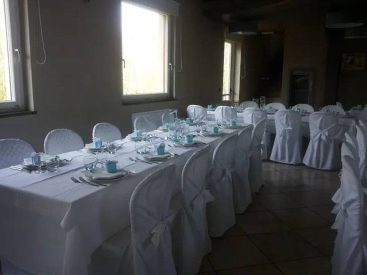 Un lungo tavolo da banchetto apparecchiato con tovaglie bianche e sedie in una sala da pranzo scarsamente illuminata.