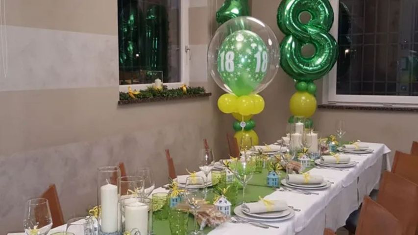 Tavolo da banchetto all'aperto decorato con centrotavola di palloncini verdi e segnaposto per una festa.