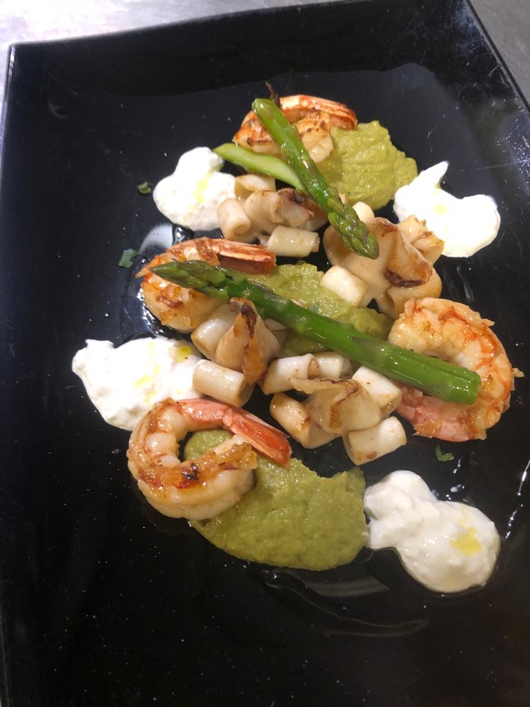 Piatto di gamberi con asparagi, verdure a dadini e salsa verde, servito su un piatto quadrato nero.