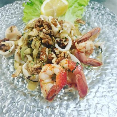 Insalata di mare con gamberi, calamari, erbe aromatiche e uno spicchio di limone su un piatto di vetro.