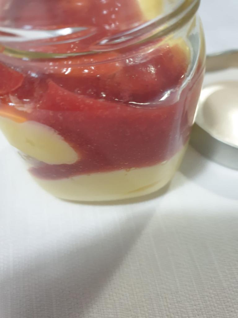Vasetto di vetro con dessert a strati rossi e gialli, ricoperto da una lucida salsa alla frutta.