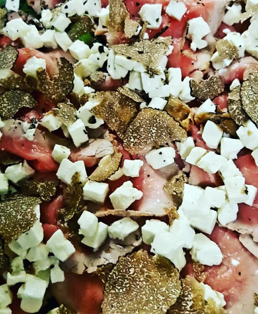 Primo piano di una pizza guarnita con formaggio a cubetti, pezzi di pomodoro ed erbe aromatiche.