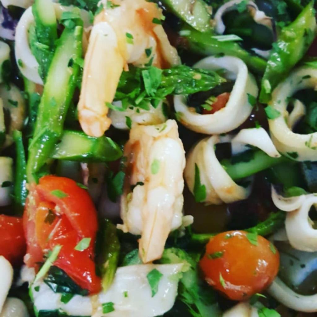 Primo piano di pasta con verdure e frutti di mare, zucchine, pomodorini ed erbe aromatiche.