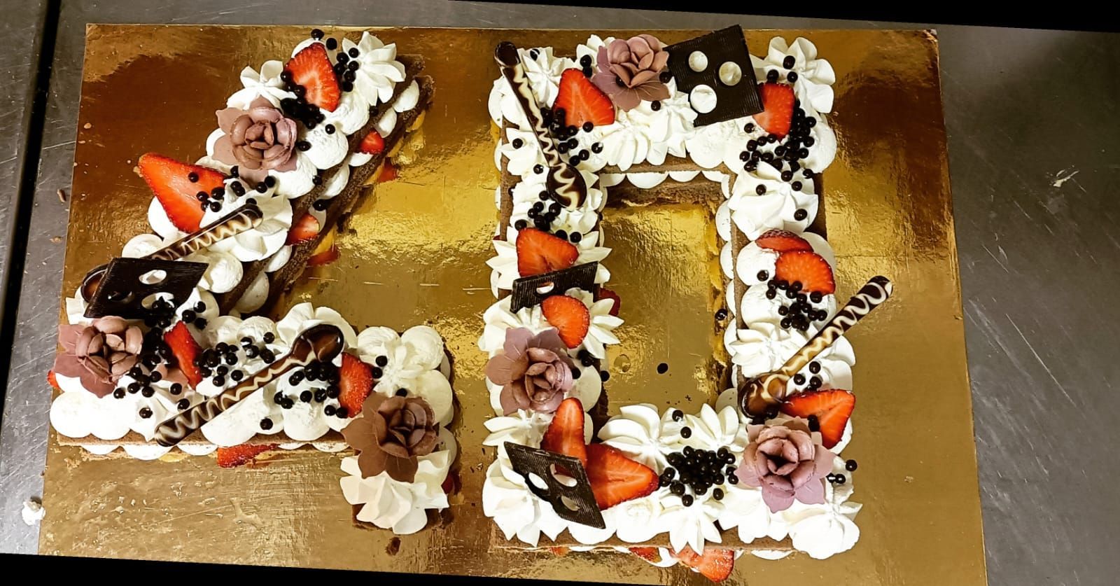 Torta di compleanno a forma di numero, decorata con fragole, panna montata e glassa al cioccolato, su un vassoio dorato.