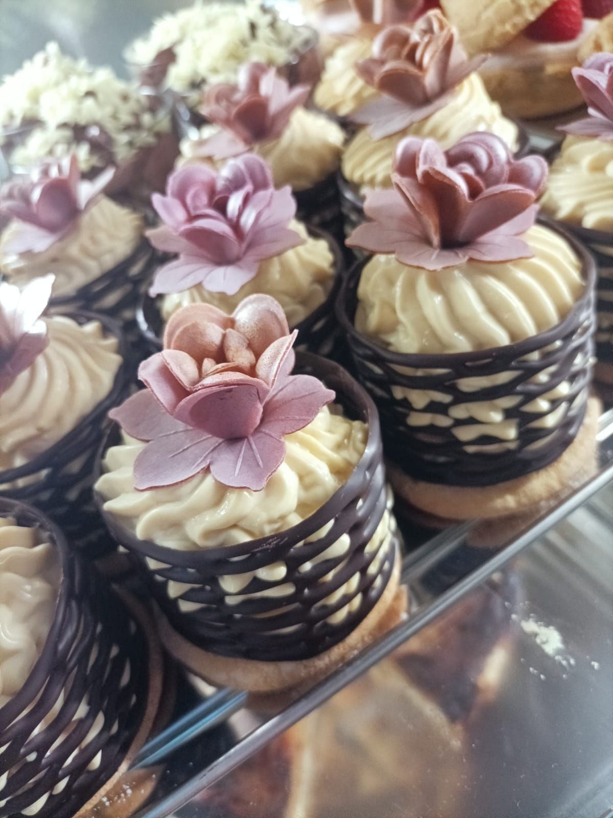 Assortimento di cupcake decorati con fiori rosa e glassa alla crema, esposti in una vetrina da pasticceria.