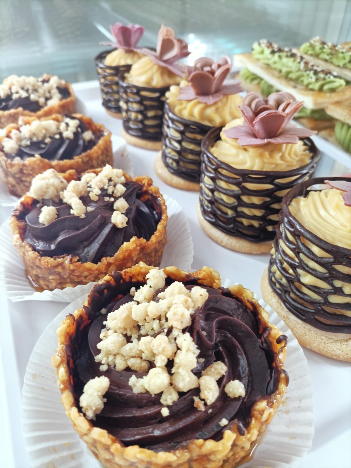 Coppette da dessert assortite decorate con volute di cioccolato, panna e briciole, disposte su un vassoio.