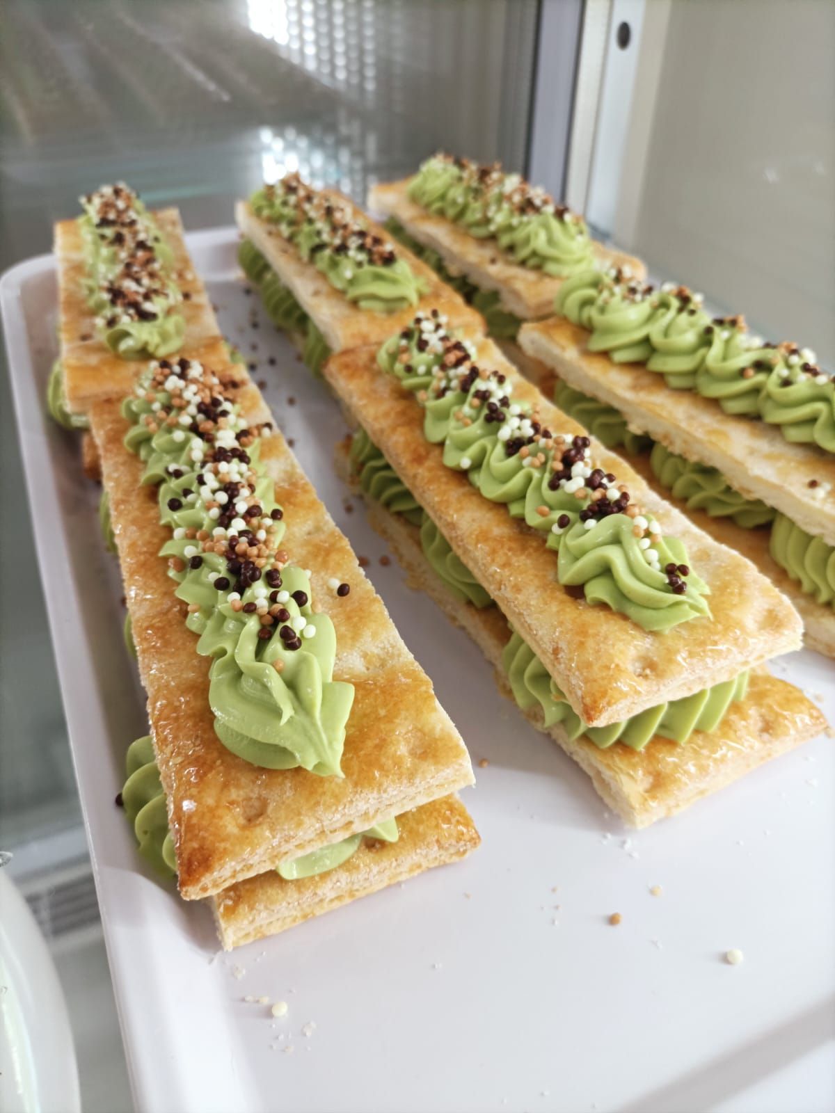 Tre barrette di dessert ricoperte di glassa verde e guarnite con frutta secca tritata, disposte su un vassoio bianco.
