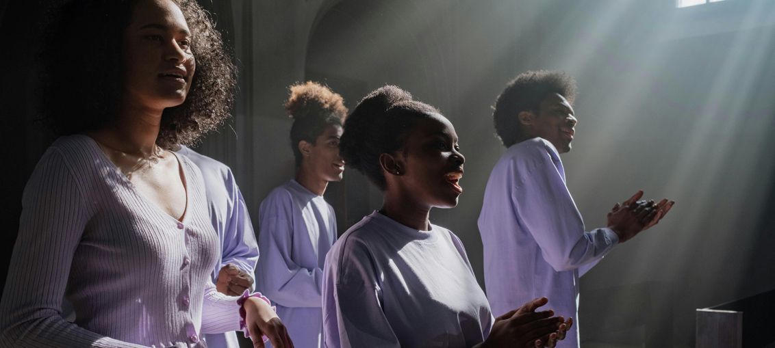 People in light-colored shirts stand in sunlight, some with hands raised in a room.