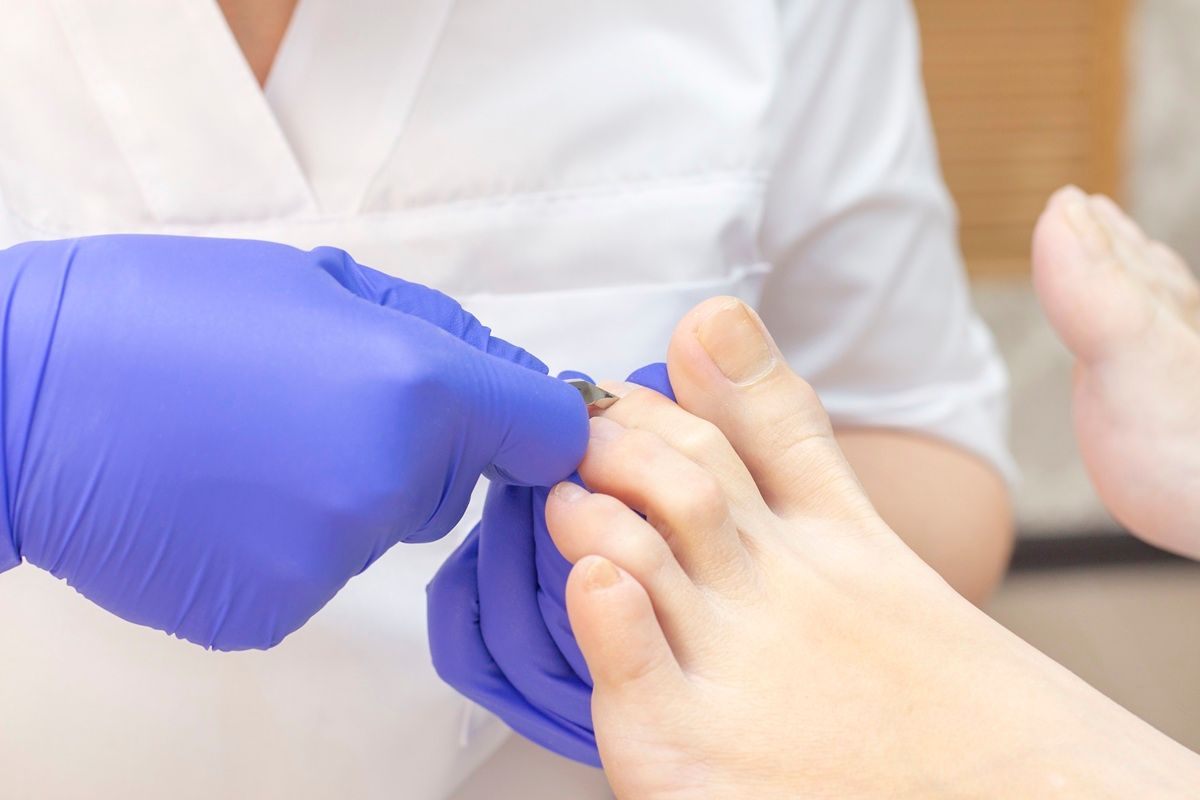 Gloved hands painting a toenail on a foot in a salon setting