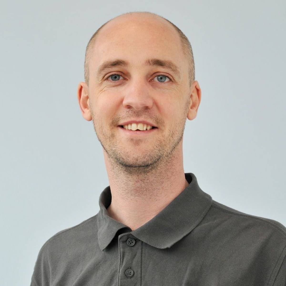 Smiling bald man in a gray polo shirt against a light background