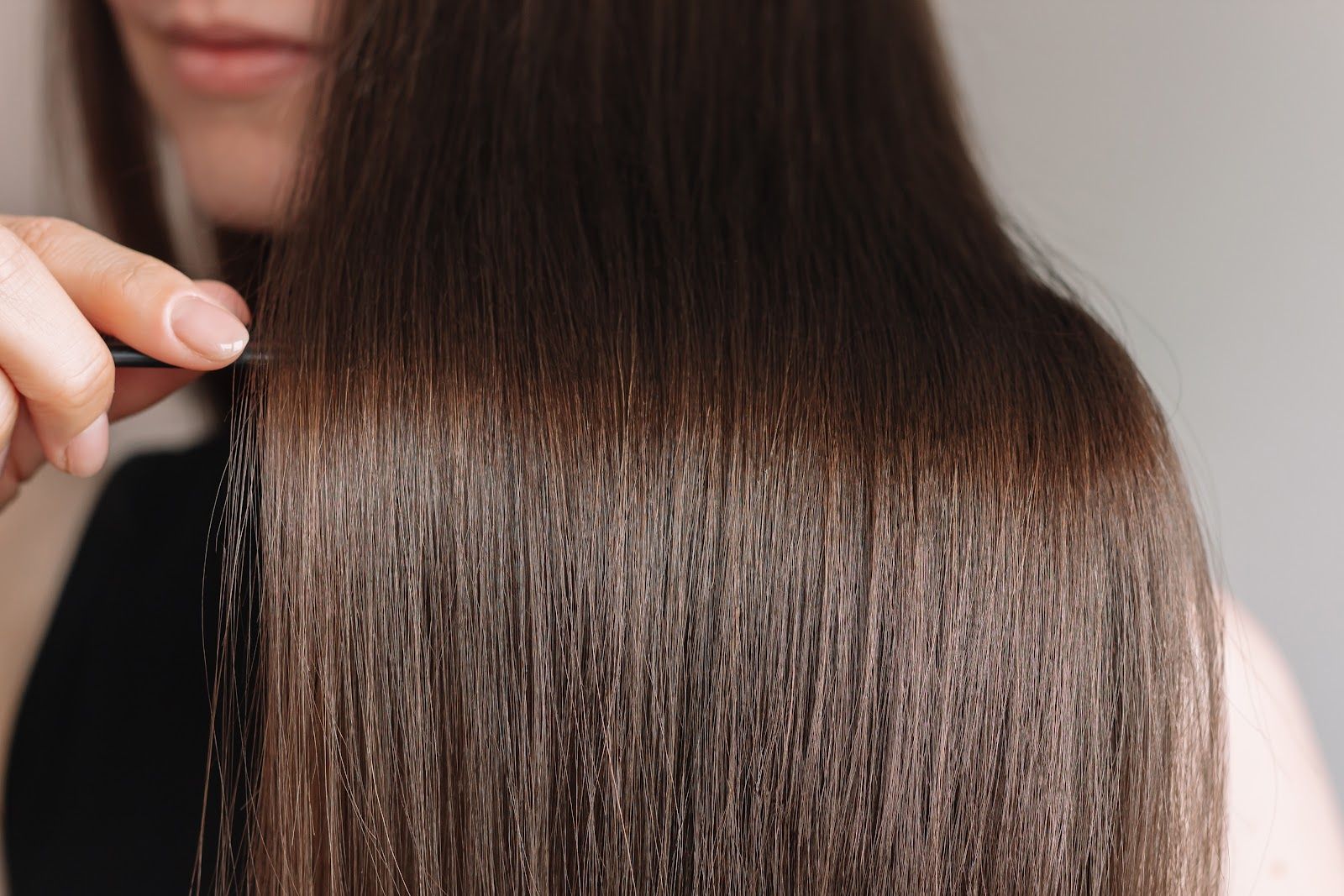 Hand holding a section of smooth, straight dark brown hair with a glossy finish