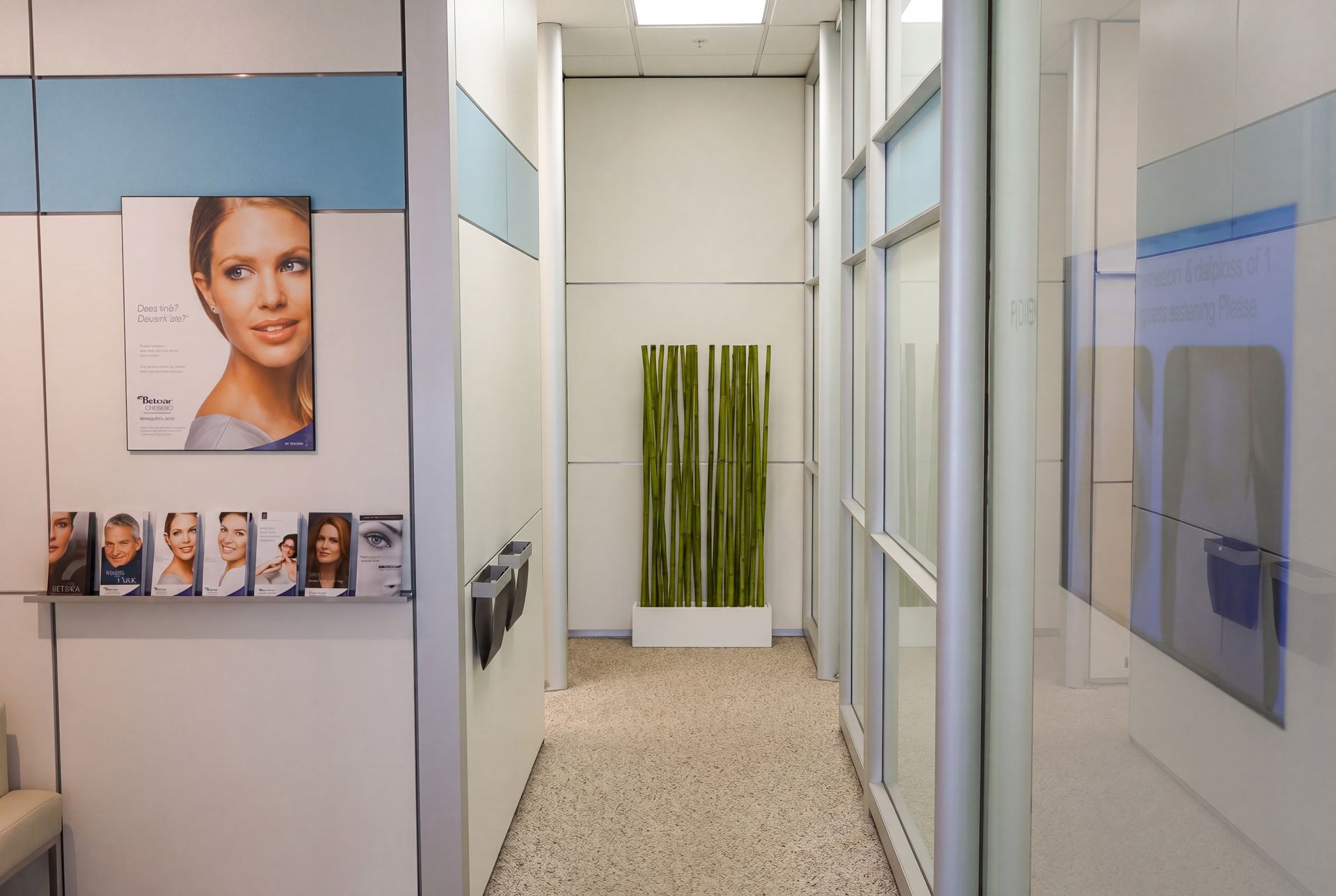 Narrow clinic hallway with posters on the left, frosted glass on the right, and a green plant artwork at the end.