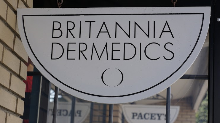 White storefront sign reading “BRITANNIA DERMEDICS” with a semicircle design underneath.