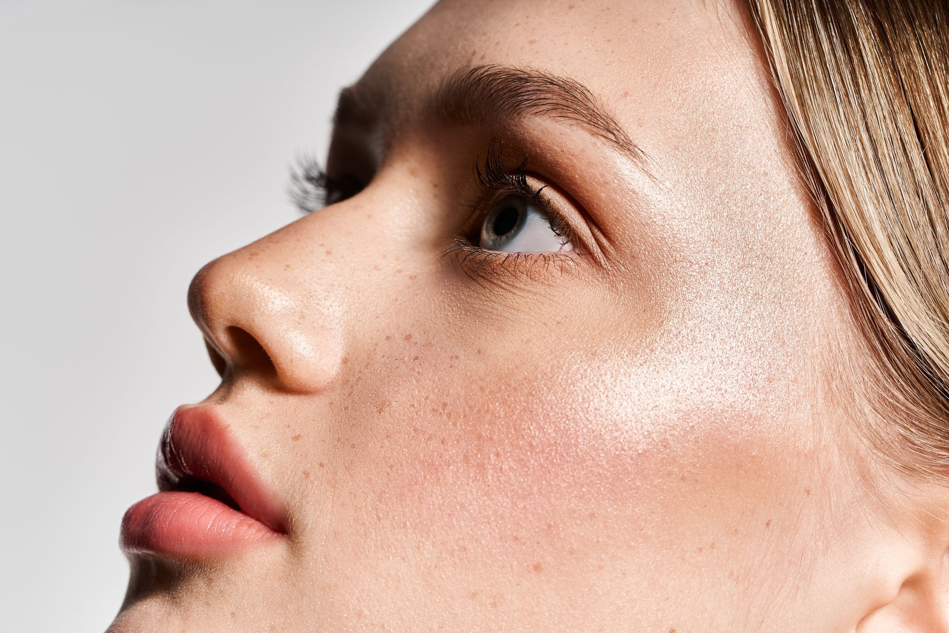 Close-up side profile of a person with fair skin and blonde hair, looking upward against a light background