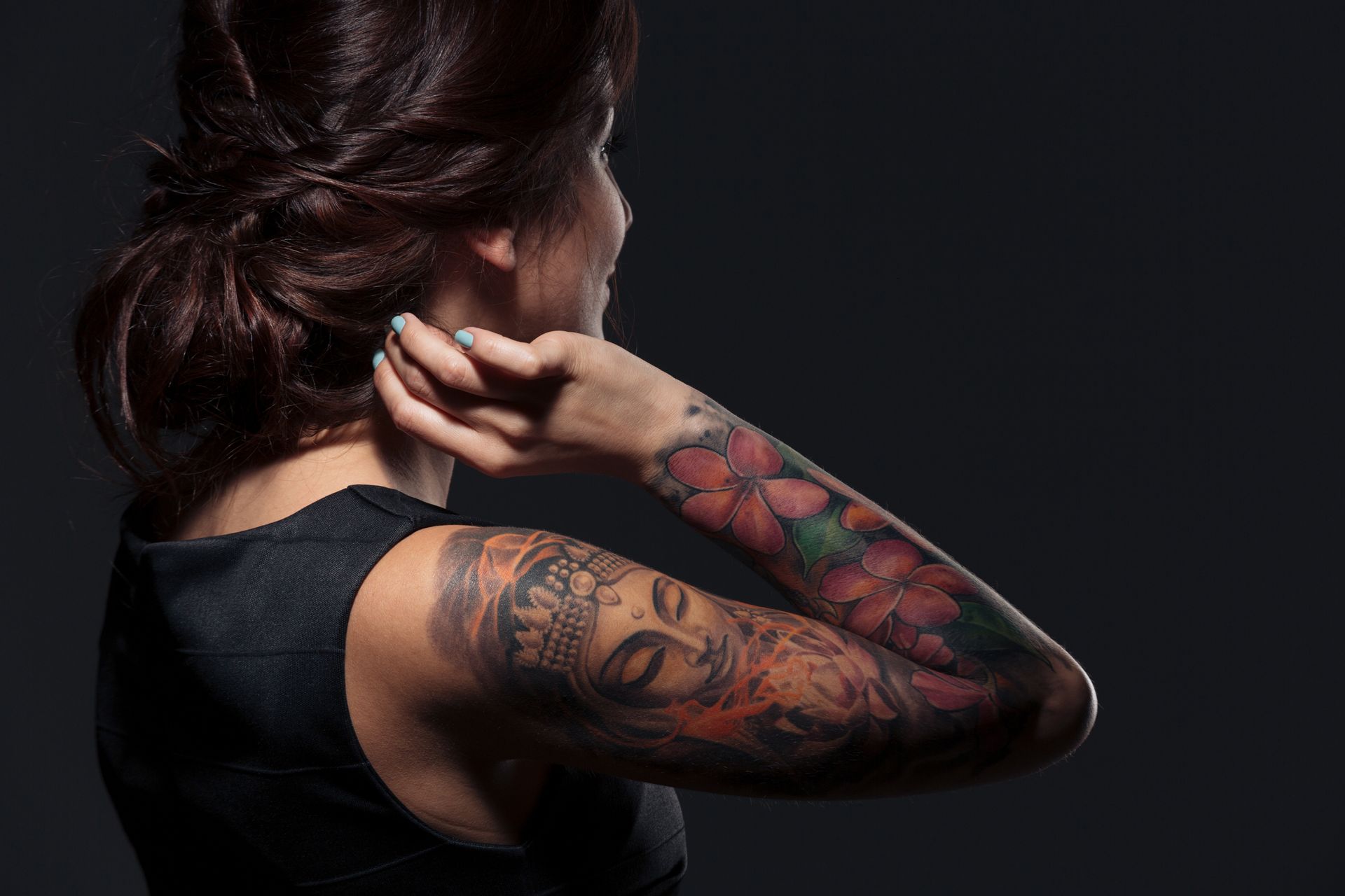 Woman with full sleeve tattoos, arm raised near head, dark background.