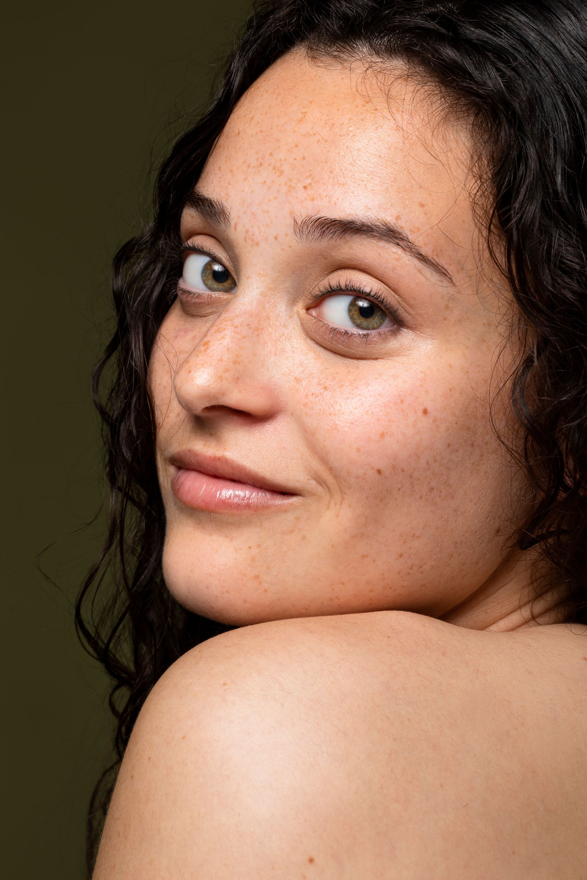 A woman with curly hair is looking over her shoulder at the camera.