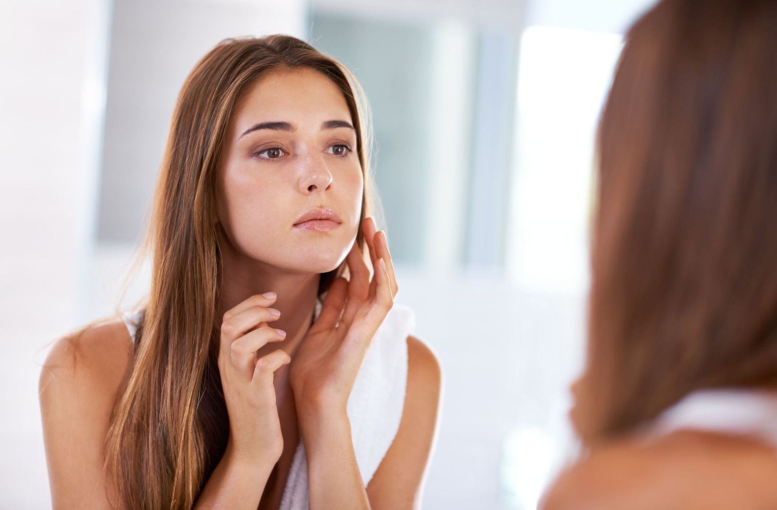 A woman is looking at her face in the mirror.