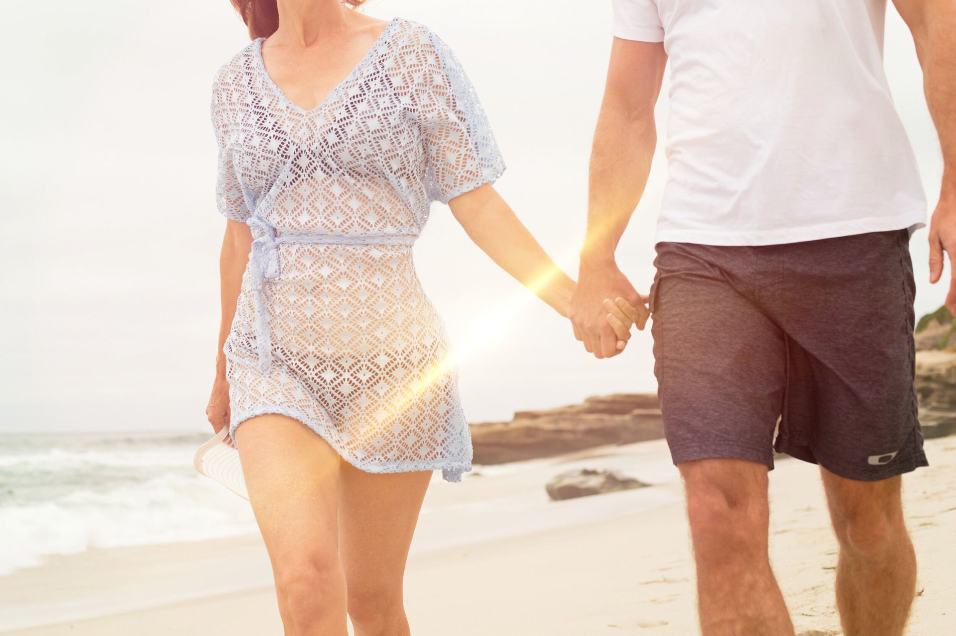 A man and a woman are holding hands while walking on the beach.