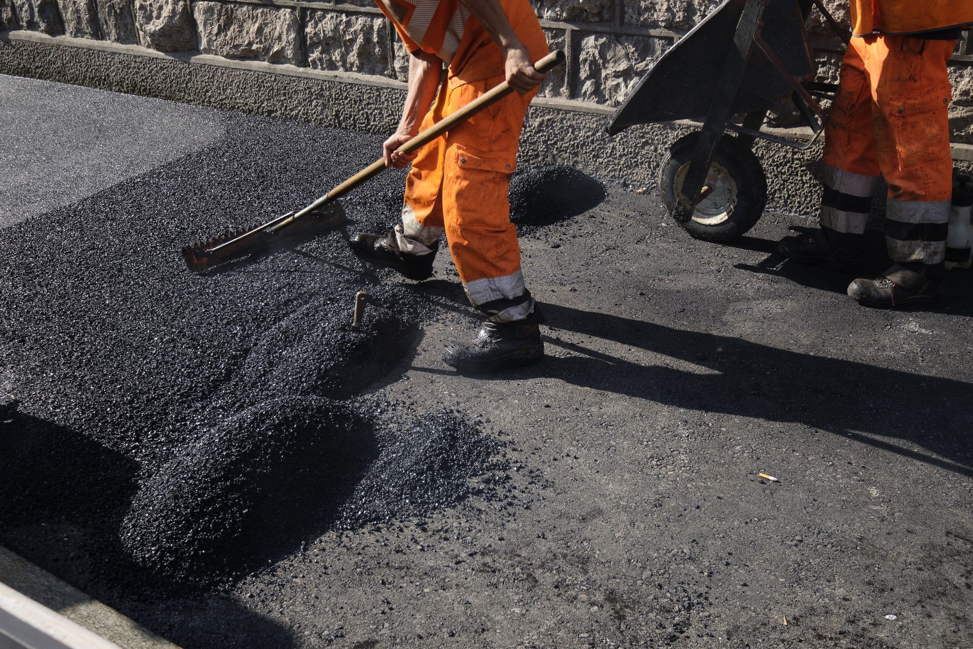 Workers are spreading asphalt with shovels and wheelbarrows during road construction. Workers are spreading asphalt with shovels and wheelbarrows during road construction.