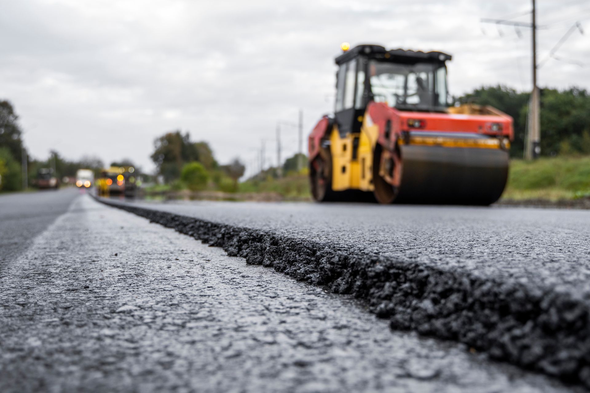 Road roller compacting fresh asphalt on a newly paved road, close-up of pavement edge